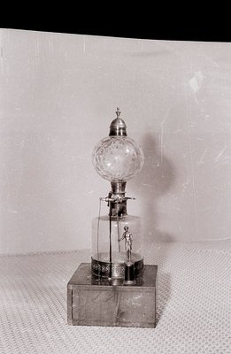 Intricate automaton depicting a miniature figure operating a bellows within a glass dome. Detailed mechanical display rests o...