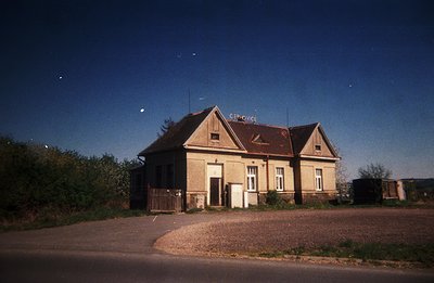 Abandoned train station building, likely in rural Central Europe. Features a gabled roof, brick facade with simple windows, a...