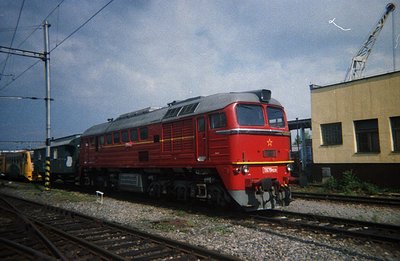 A powerful, red Soviet-era diesel locomotive (likely a TE3 series) sits on tracks, coupled to freight cars. The locomotive nu...