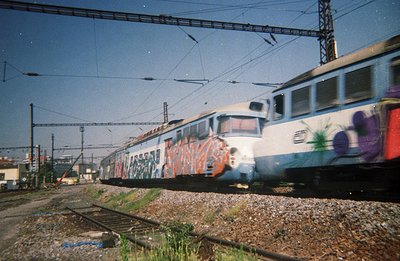 A high-speed passenger train, likely electric, speeds along tracks with vibrant graffiti covering its exterior. The scene sug...