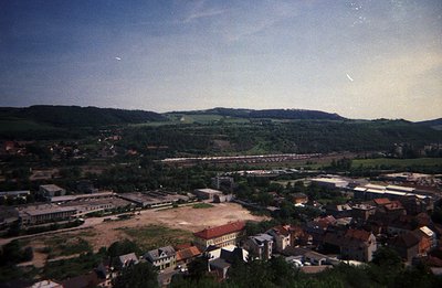 Elevated view of a town featuring red-roofed buildings, a rail yard, and a wooded hillside landscape. Likely a post-industria...