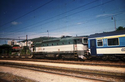Locomotive and passenger car on railway tracks. The locomotive, with a teal and white livery, appears to be a Bulgarian State...