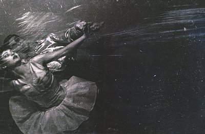 A dynamic, blurred monochrome photograph captures a dancer in mid-motion, likely a pirouette. The dancer wears a tutu and bal...