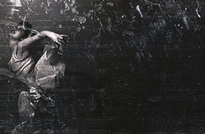 Striking, dramatic dance portrait of a figure in mid-motion, likely female, with flowing fabric emphasizing movement. Grainy ...