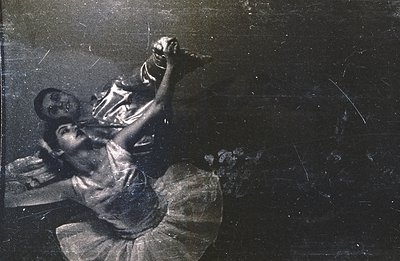 A dancer in a flowing gown is captured mid-performance, seemingly lifted by a partner who is mostly obscured. The image exhib...