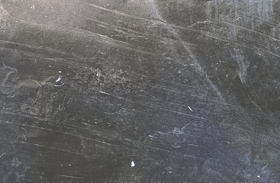 Dust and scratches across a dark grey surface dominate this image. The texture suggests aged photographic film or an oxidized...