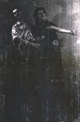 A formal portrait captures a couple in vintage attire. The man wears a patterned suit, while the woman is in a beaded dress a...