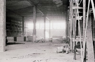 Striking black and white photo depicts a construction site interior. Concrete pillars and scaffolding dominate the view, hint...