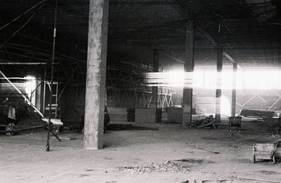 An interior view depicts a construction site, likely unfinished. Concrete pillars support a timber-framed roof structure. Lum...