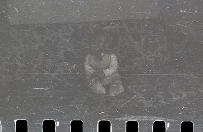 A blurred figure appears on a strip of 35mm film, showcasing noticeable dust and scratches characteristic of aged photographi...