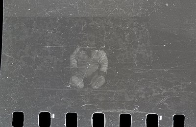 A grainy, partial image of a person's hands in a dark coat, captured on aged 35mm film stock. Visible sprocket holes indicate...