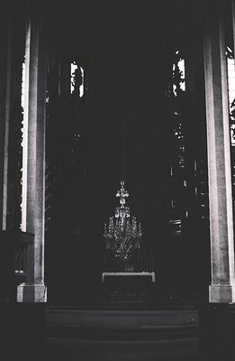 Grand, ornate chandelier hangs within a darkened, neo-classical interior. Dramatic vertical lines of columns frame the scene....