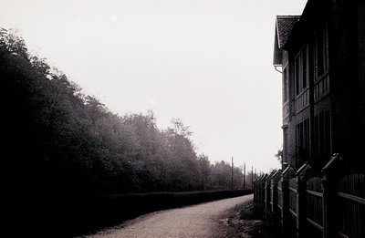 A monochrome view depicts a weathered building with dormer windows and a steeply pitched roof, bordered by a low, ornamental ...