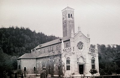Grand Romanesque-style church with a tall, square bell tower. Detailed stone facade, arched windows, and a prominent rose win...