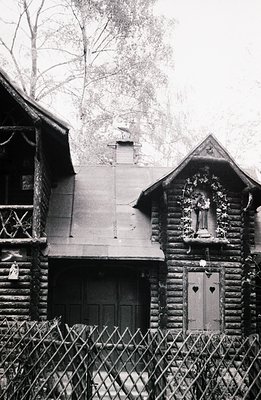 Rustic, timber-framed building with a small shrine niche featuring a statue, likely a religious icon. Heart-shaped windows an...