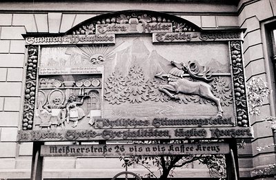 Elaborate stone relief advertisement displays a stylized alpine landscape with a leaping stag and a figure carrying beer barr...