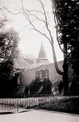 A black and white photograph captures a stately villa with a distinctive conical roof and ornate window detailing, set within...
