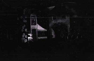 Vintage photograph depicting a young girl standing amidst a stylized, almost theatrical landscape. Features a fabricated buil...