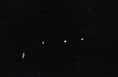 Image depicts a black surface with multiple prominent light leaks and dust spots scattered across the frame. The texture sugg...