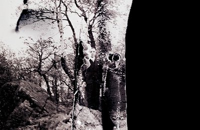 Striking black and white photo depicts a weathered, abstract view through a partially obscured window. Treeline & rocky hills...