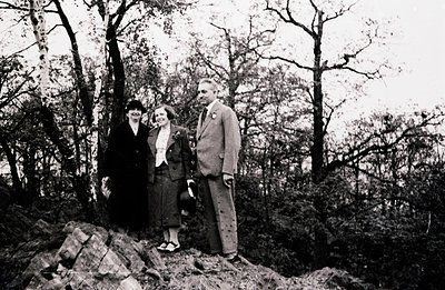 A formal portrait of three individuals posed on a rocky hillside, likely a family or group of friends. The subjects are dress...