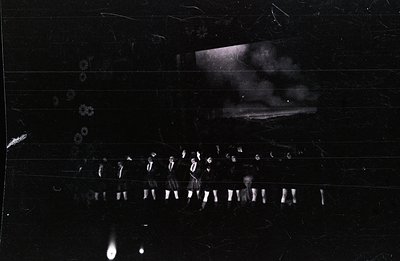 A group of formally-dressed men stand in a row, possibly military or uniformed personnel. The scene appears staged, with a bl...