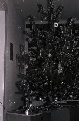 A festive, flocked artificial Christmas tree, heavily adorned with silver tinsel and ornaments, dominates this indoor scene. ...