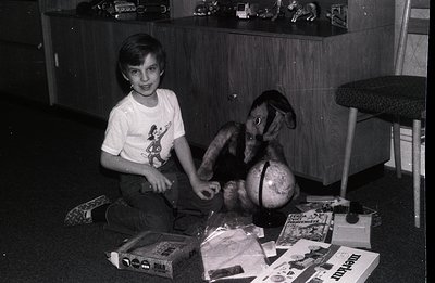 Young boy seated amid toys & gifts, including a plush deer and globe, surrounded by wrapped presents. Appears to be a domesti...