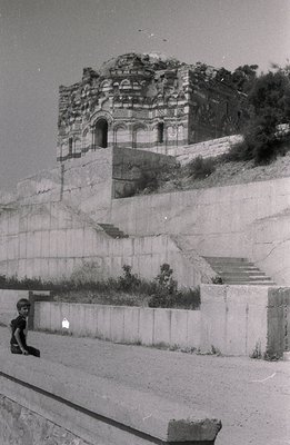 An elevated, partial view of a historic ruin, possibly a church or temple, sits atop a terraced hillside. A small boy in shor...