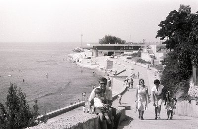 A black and white view of the Varna seaside resort in Bulgaria. A man cradles a child on a concrete retaining wall overlookin...