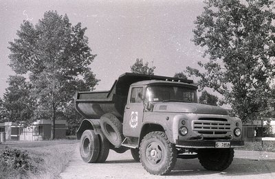 Heavy-duty Soviet-era dump truck, likely a Ural model, parked on a gravel road amidst sparse vegetation. Features include a p...