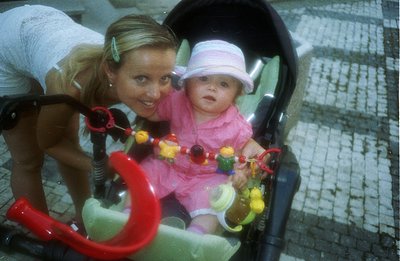 A young woman with blonde hair, styled in a high ponytail, gazes down at a baby seated in a vibrant green stroller. The baby ...