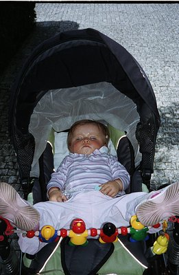 Infant rests peacefully in a travel stroller, sheltered by a mesh sunshade. Soft pastel stripes adorn the baby's sleepwear. A...