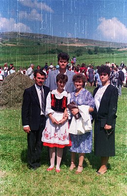A family portrait shows a man in a suit, a young woman in traditional folk dress, and two women in dresses and suits, posed i...