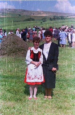 Two women stand in a grassy field during what appears to be a cultural festival. The woman on the left wears a traditional em...
