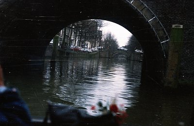 View of a canal scene framed by a brick archway. Traditional Dutch architecture lines the water's edge, reflected in the stil...