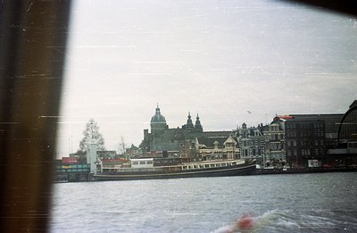 A passenger boat travels along a canal, passing ornate 17th-century Dutch architecture, likely in Amsterdam. The scene is cap...