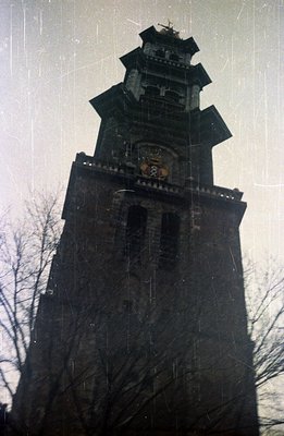 A tall, multi-tiered brick tower with decorative stonework and a pointed roof dominates this photo. A crest or emblem is visi...