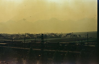 A color photograph depicts a landscape with a railway line in the foreground and distant mountains in the background. Several...