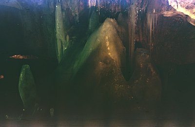A view within a grotto or cavern, showcasing textured rock formations illuminated by dramatic, directional lighting. Visible ...