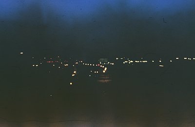 Long-exposure view of a string of lights along a shoreline, possibly a pier or walkway, with what appear to be buildings illu...