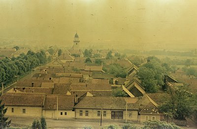 A high-angle view showcases a European village with tightly packed, red-tiled roofs. A church steeple rises above the buildin...