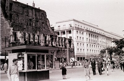 Wartime destruction contrasts with the intact, modernist apartment building façade. A damaged structure exposes brickwork and...