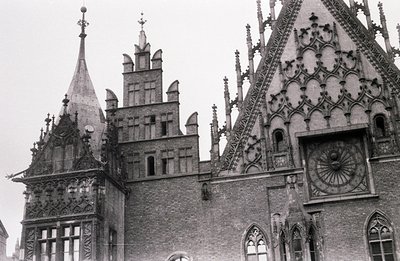 A black and white photograph showcases intricate Gothic Revival architecture. A central spire rises above a complex brick fac...