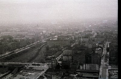 Overcast view of a city, likely industrial, with rail lines bisecting the scene. Dense atmospheric haze obscures distant stru...