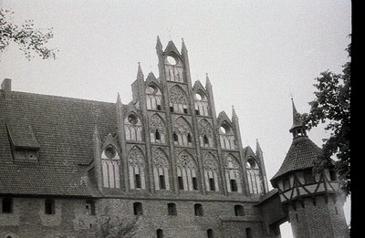 Striking Gothic-style brick facade of a medieval castle, showcasing intricate tracery and pointed arches. The roofline is ste...