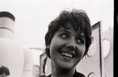 Close-up portrait of a young woman with short, dark hair, smiling widely and looking off-camera. Grainy black and white image...