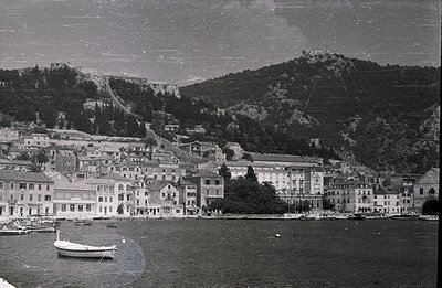 Seaside townscape with tiered architecture, likely Adriatic region. Buildings exhibit classical detailing & balconies. A smal...