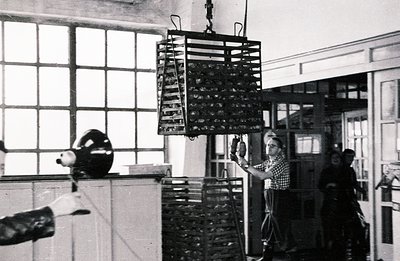 Industrial interior featuring a large, suspended wire rack possibly used for drying or processing. Two workers, one visible f...
