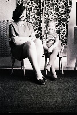 Black and white image featuring a seated woman and child. The woman wears a short-sleeved dress and necklace, the child a str...